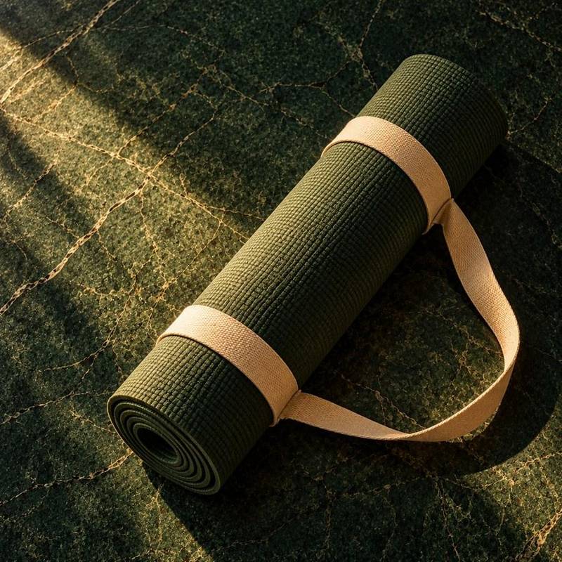 A rolled green yoga mat with a cream strap, in warm morning light